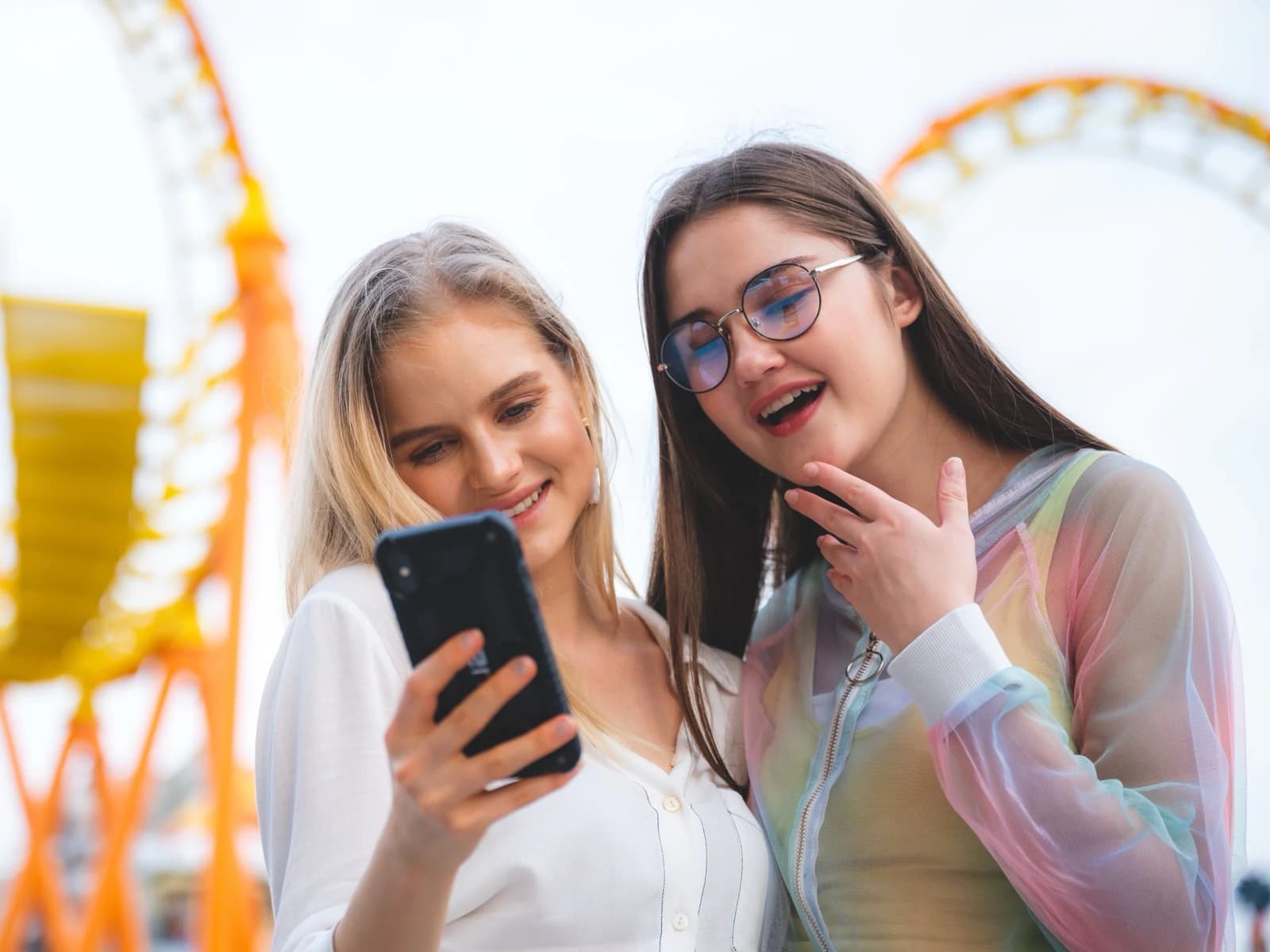 Zwei Freundinnen in einem Freizeitpark schauen gemeinsam auf ein Smartphone
