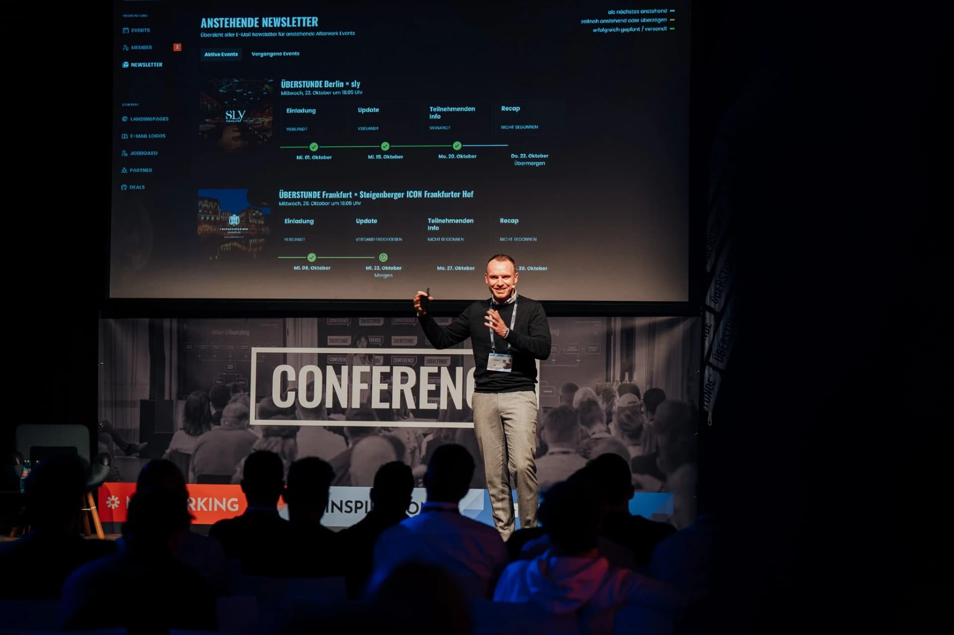 Raphael Mis auf der Bühne einer ÜBERSTUNDE-Konferenz, hinter ihm die Newsletter-Übersicht des ÜBERSTUNDE-Dashboards