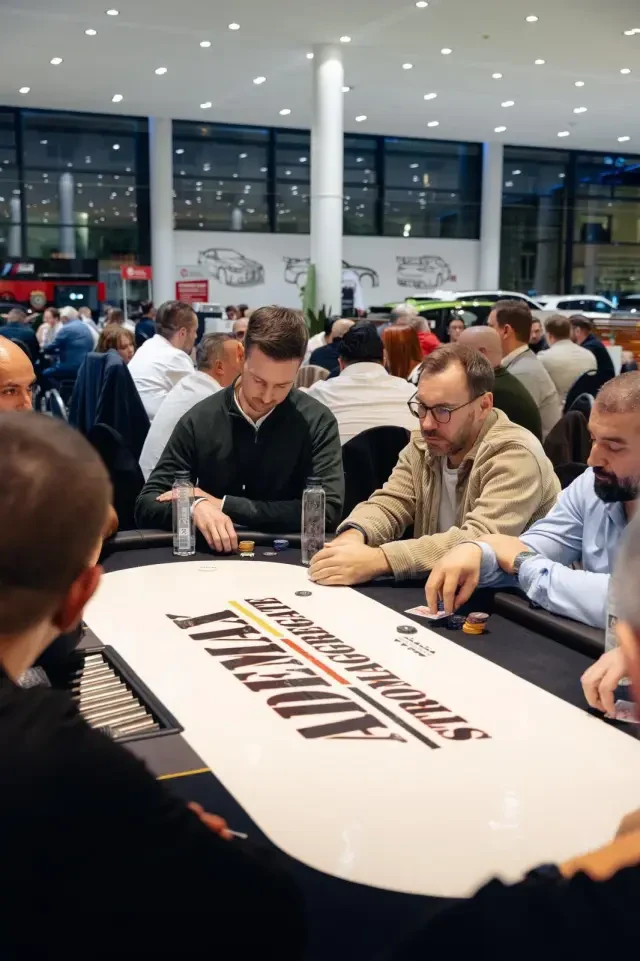 BusinessPokern-Abend in einem Autohaus: Gäste konzentriert am Pokertisch, dahinter weitere Tische und Fahrzeuge