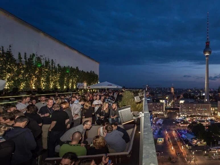 ÜBERSTUNDE in Berlin: Gäste auf einer Dachterrasse am Abend